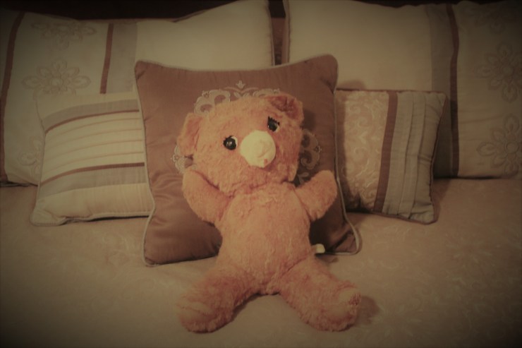 very old teddy bear leaning against bed pillows